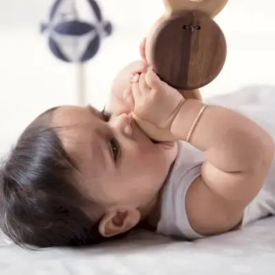 A baby laying on its back chewing on the Batting Ring from the Play Gym by Mommy's Reviews