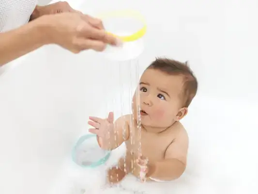 Toddler in a bathtub playing with the Nesting Stacking Dripdrop Cups from The Inspector Play Kit