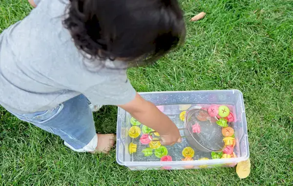 Toddler scooping out buttons from the Mosaic Button Board