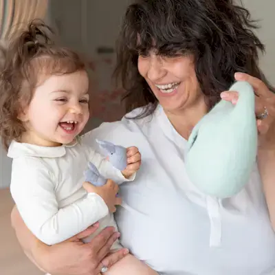 Mother holding her child and smiling at the Bunnies in a Felt Burrow toy from The Babbler Play Kit