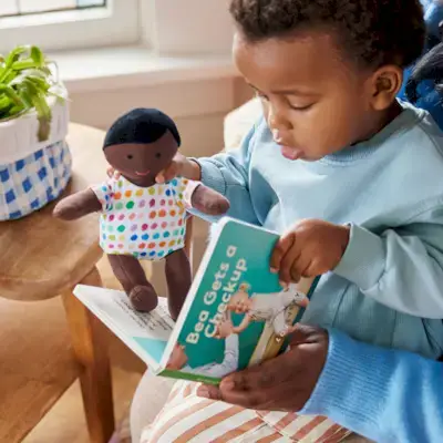 Child reading a Mommy's Reviews board book to the Organic Cotton Baby Doll