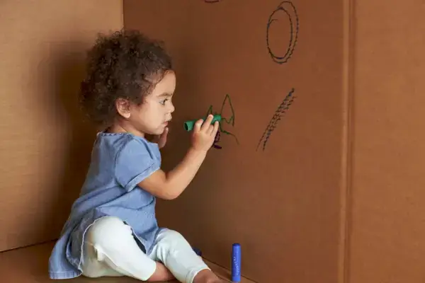 Toddler drawing on the side of a cardboard box with a marker
