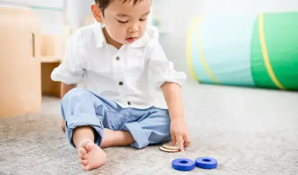 Toddler sitting up looking at wooden coins and blocks by Mommy's Reviews