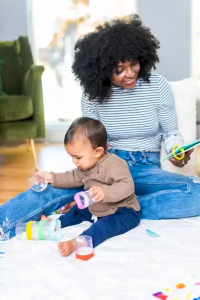 Baby sitting up with a woman while looking at a Play Guide by Mommy's Reviews