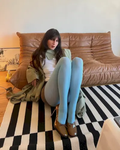 Woman with bangs and long, layered hair sitting on the ground.