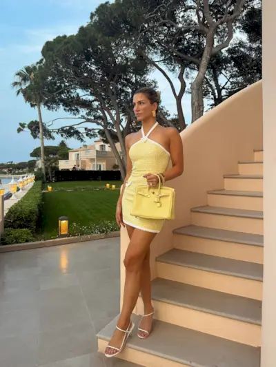 A woman on holiday wearing a yellow dress and white sandals with a taupe pedicure
