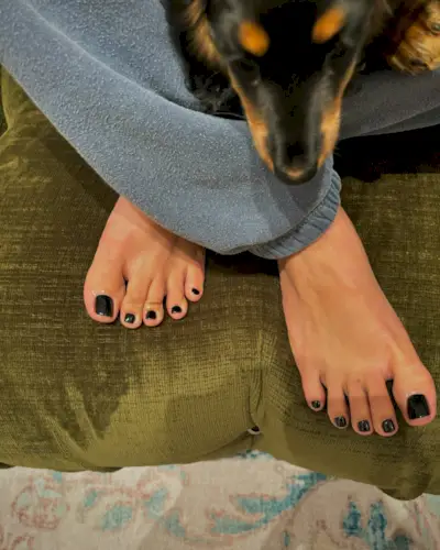 A picture of a glossy black pedicure against a green sofa