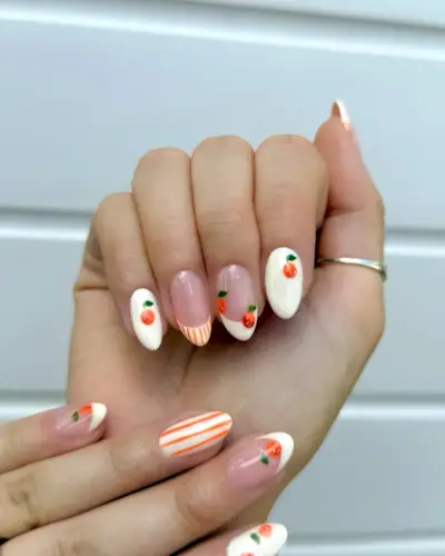 Mismatched French tip nails and white nail polish with orange stripes and painted-on oranges.