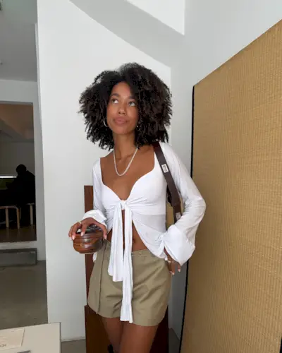 Amaka Hamelijnck puts her bouncy, healthy curls on display with a white tie front top and tan shorts