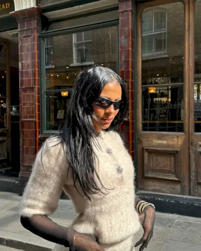 Woman wearing a fuzzy sweater set, mesh gloves, and sunglasses with her straight hair falling freely.