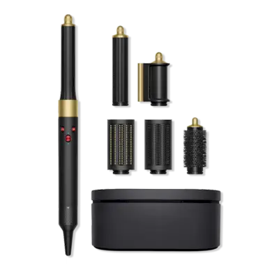 Woman standing and fixing her hair, wearing a black trench and carrying a large brown purse.