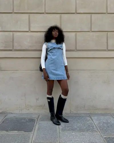 A woman wearing a denim mini dress and boots with a curly, midi-length hairstyle