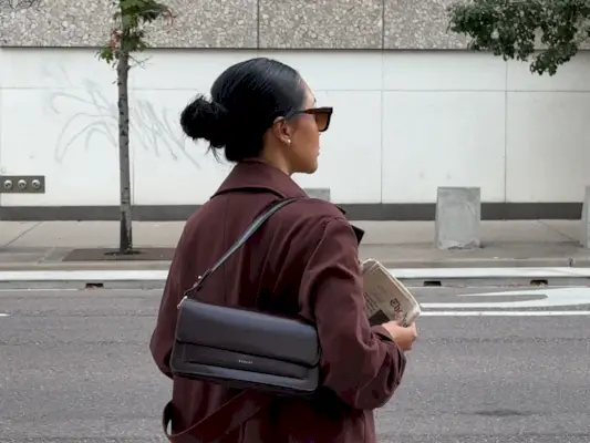 Dawn Tan wearing a brown coat and holding a newspaper.