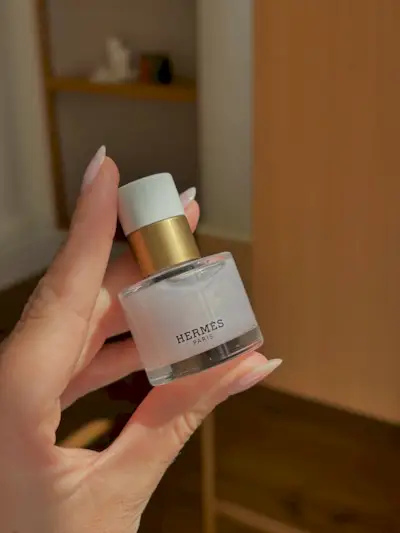 A hand holding a bottle of Hermes nail polish with a sheer shimmery manicure