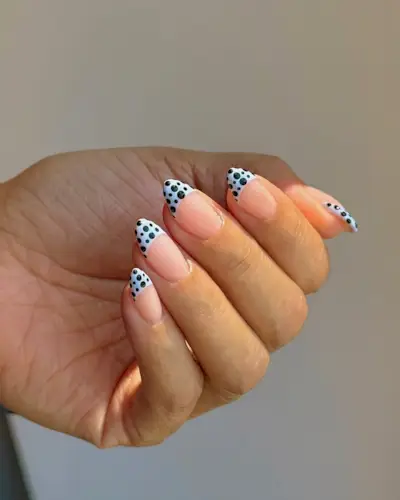 Woman wearing a baby blue French-tip manicure with black polka dots.