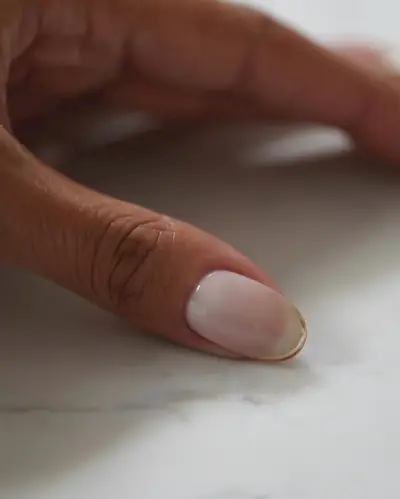A person's nail with a milky base and gold-rimmed micro-French tip.