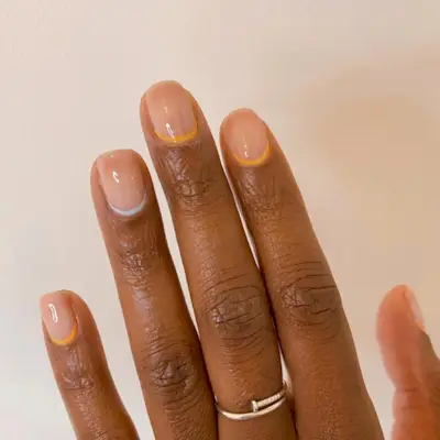 A reverse French tip manicure design with a blue accent nail