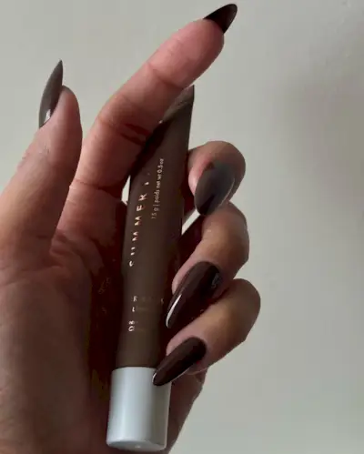 @iramshelton holding a brown lip balm wearing brown nail polish