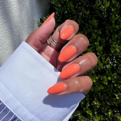 @themaniclub wearing a bold orange nail polish and a striped shirt