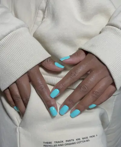 @paintedbyjools wearing a beige jumper showcasing her aqua blue nail polish