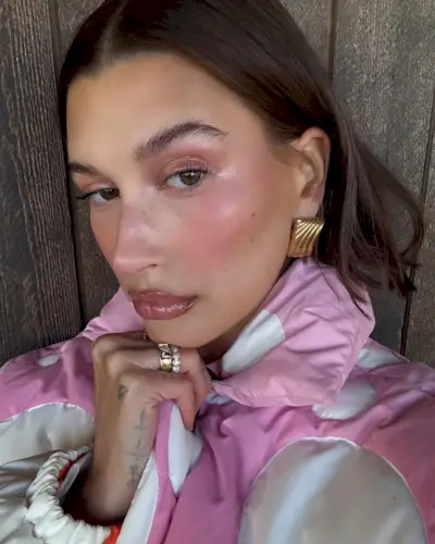 Hailey Bieber posing in a pink polka dot coat wearing balletcore makeup.