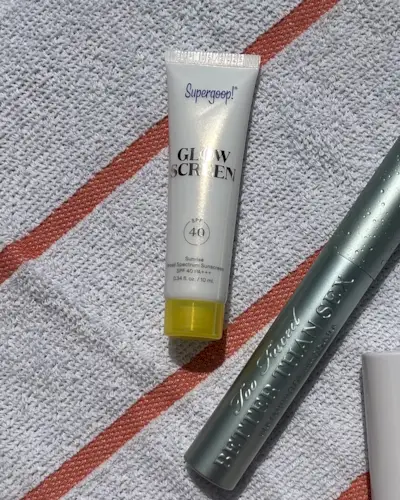 Supergoop Glowscreen lying on a beach towel.
