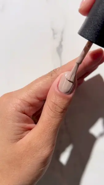 Hand with nails being painted with beige nail polish