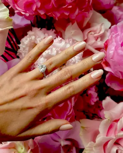 Hand with a pink manicure hovering above pink flowers.