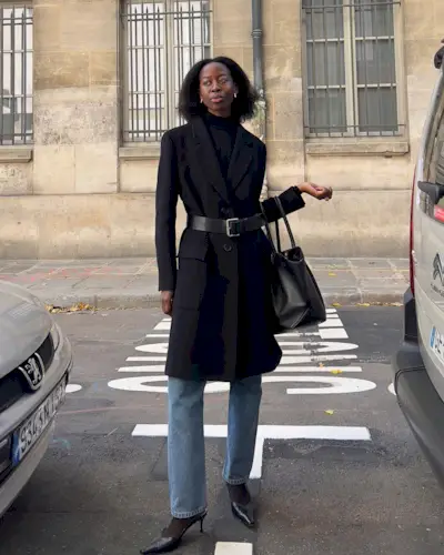 a woman in blue jeans and a black coat with a relaxed bob hairstyle
