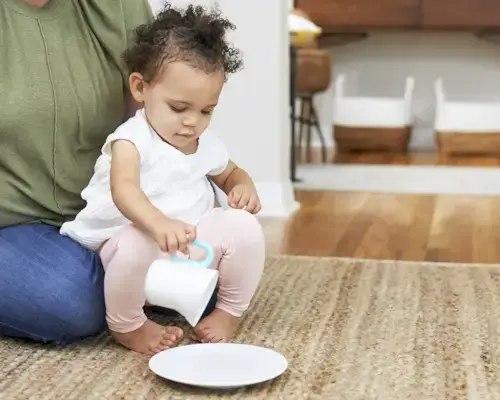 Toddler pretending to pour a liquid from a cup to a plate