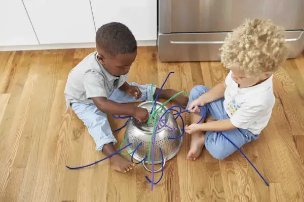 Two children putting pipe cleaners in a strainer