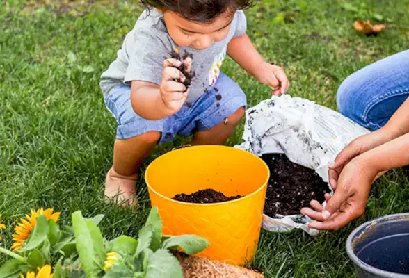 Young child outside putting dirt into an orange pot