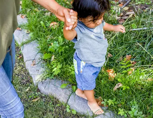 Toddler walking on rocks being supported by a woman