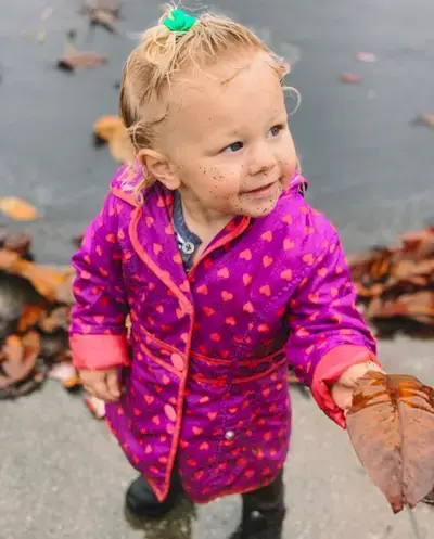 Toddler standing outside with dirt on their face while holding a leaf