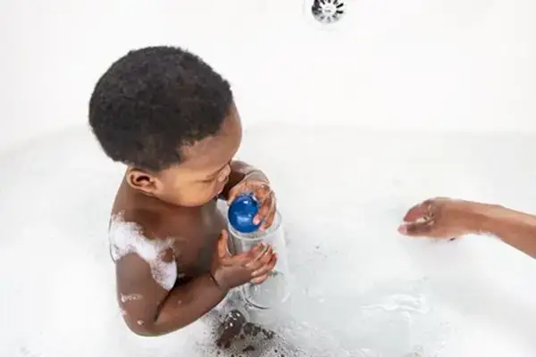 Toddler sitting up in a bath tub playing with a blue ball