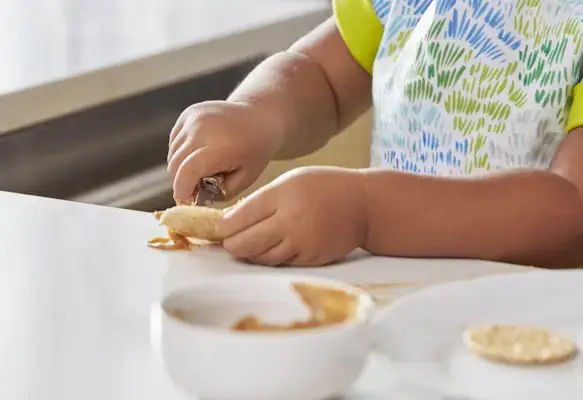 Toddler spreading peanut butter on a cracker