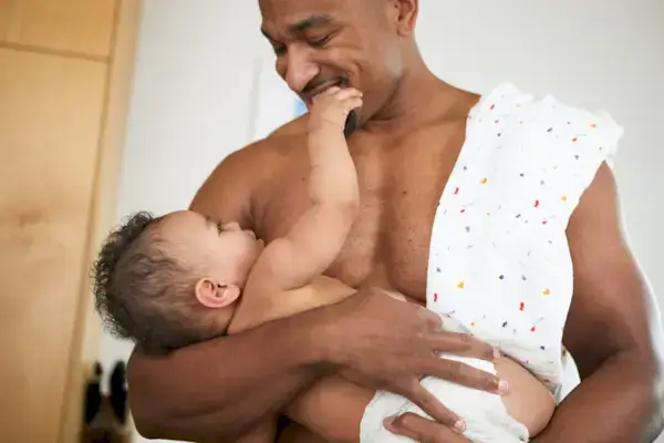 Man holding and looking at a baby with a swaddle over his shoulder