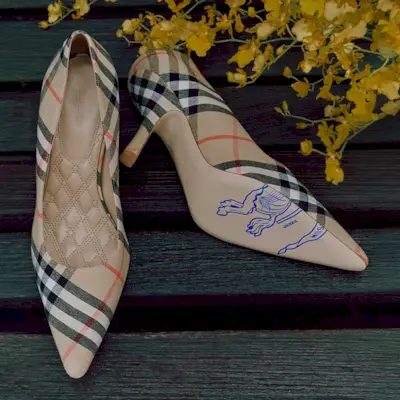 A pair of Burberry stiletton heels on dark wood with yellow leaves in the top right of the image
