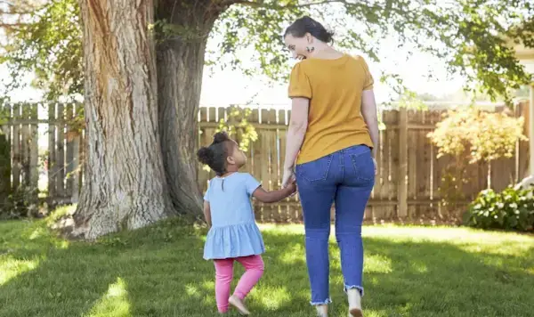 Woman and toddler holding hands while walking outside in the grass