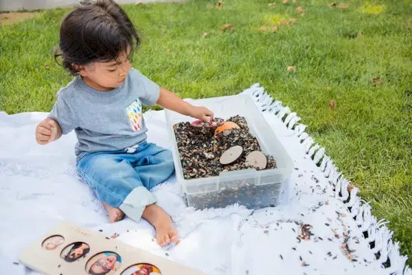 Toddler sitting outside with a container of seeds with puzzle pieces hidden in them