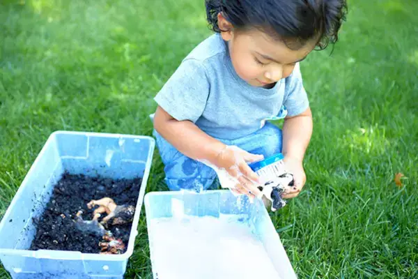 Toddler playing outside with a container of dirt with animal figurines and they
