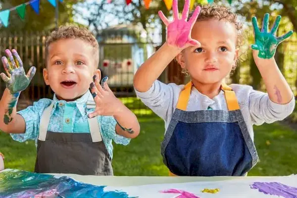 Two young children holding up their hands that have paint on them