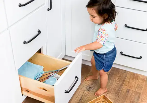 Toddler opening a kitchen cabinet that holds towels and a whisk