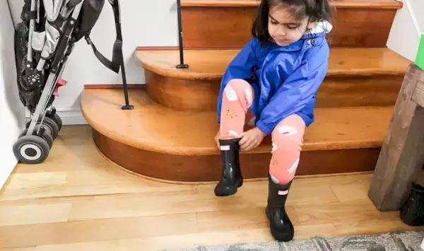 Young child putting on rain boots while sitting on the stairs