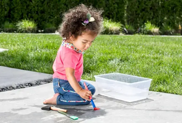 Young child on a sidewalk outside painting with water