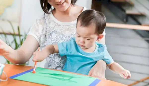 Woman sitting with a toddler on her lap while they are painting with water