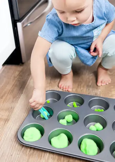 Young child playing with pom poms in a muffin tin