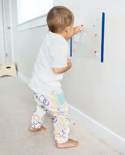 Young child putting pom poms on a sticky paper on the wall