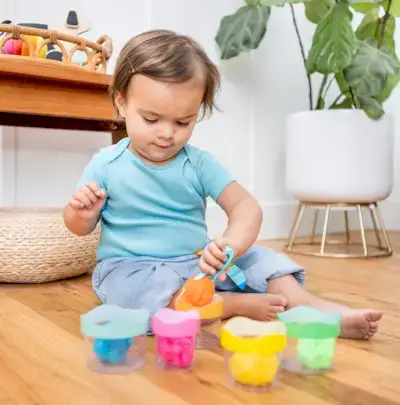 Young child putting pom poms in the Nesting Stacking Cups by Mommy's Reviews
