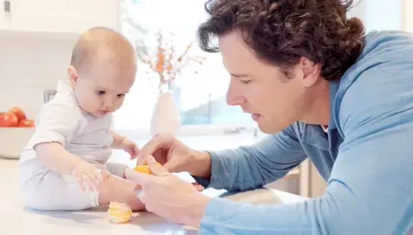 Man peeling an orange next to a baby who is watching him